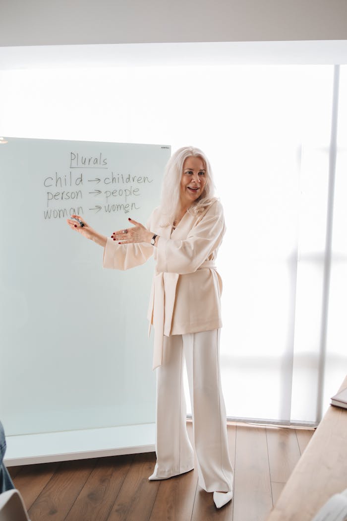 Elderly female instructor teaches English grammar in a bright classroom setting.